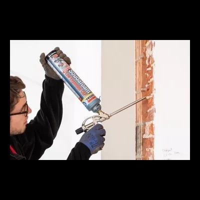 Homem usando luvas aplica espuma expansiva numa parede de tijolos