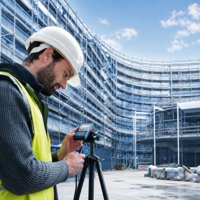 Homem com capacete e colete refletor a usar equipamento de medição digital num canteiro de obras