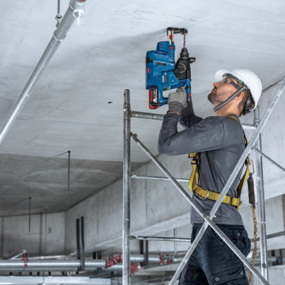 Trabalhador de construção a usar ferramenta elétrica azul no teto de betão