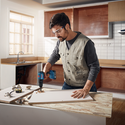 Homem a trabalhar com furadeira numa cozinha em construção.