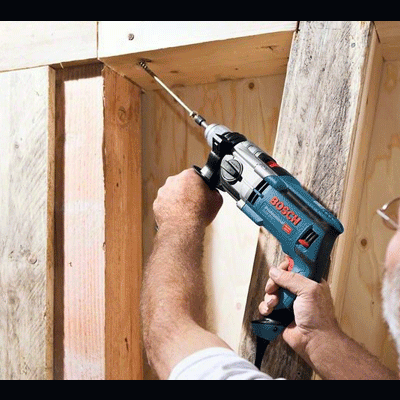 Homem usando furadeira elétrica Bosch para perfurar madeira numa construção.