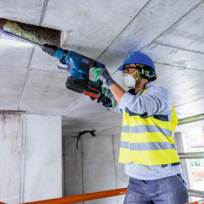 Homem a usar equipamento de proteção a perfurar teto de betão com ferramenta elétrica