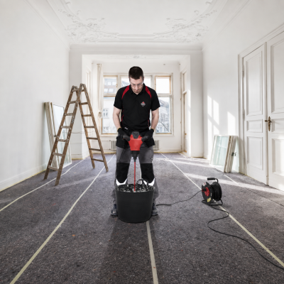 Homem a usar misturador elétrico vermelho e preto em balde numa sala em construção
