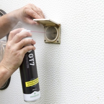 Mãos a aplicar spray GT7 num orifício circular numa parede branca