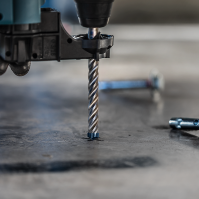 Furadeira elétrica com broca a perfurar superfície metálica ao lado de parafusos