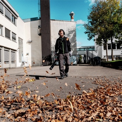 Homem usando soprador de folhas num espaço exterior urbano com edifícios e árvores