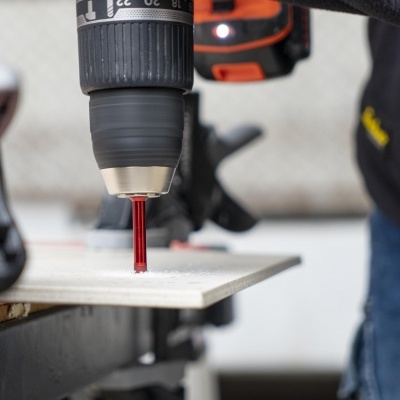 Broca vermelha em furadeira perfurando placa branca em oficina