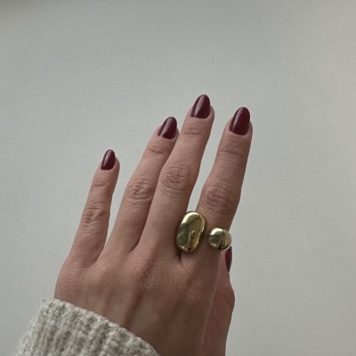 Mão com anel dourado e unhas vinho sobre fundo branco.
