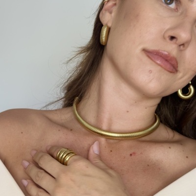 Conjunto de colar, anel e brincos dourados com textura espiral em modelo com fondo branco