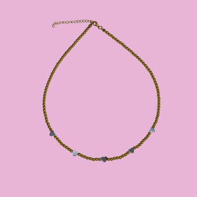 Colar dourado com detalhes em forma de coração prata sobre fundo rosa claro.