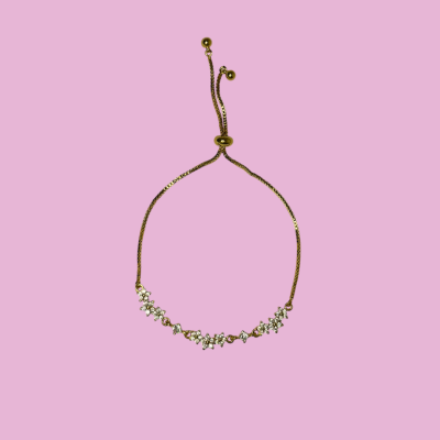 Pulseira dourada com estrelas e pedras brilhantes, fundo rosa