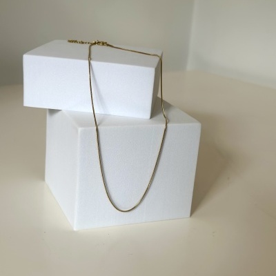 Colar dourado fino sobre caixas brancas minimalistas