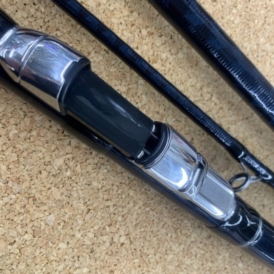 Cana de pesca preta com partes metálicas e de plástico em superfície de cortiça