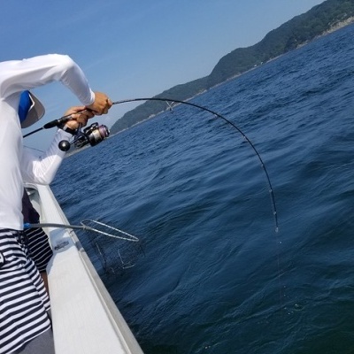 Homem a pescar vestindo camisa branca e calções às riscas num barco junto ao mar
