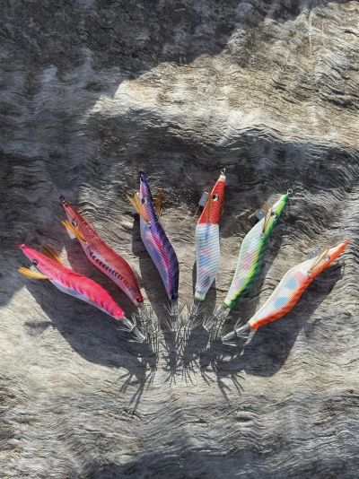 Sete iscas artificiais coloridas para pesca alinhadas em superfície cinza