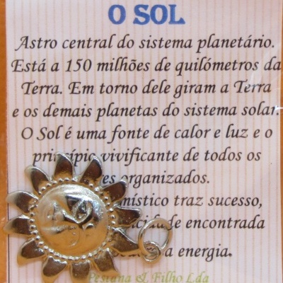 Cartão com texto sobre o Sol e pendente metálico dourado em forma de sol com olho no centro sobre fundo de madeira clara