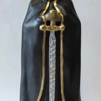 Estátua de figura encapuzada com manto preto e dourado segurando espada
