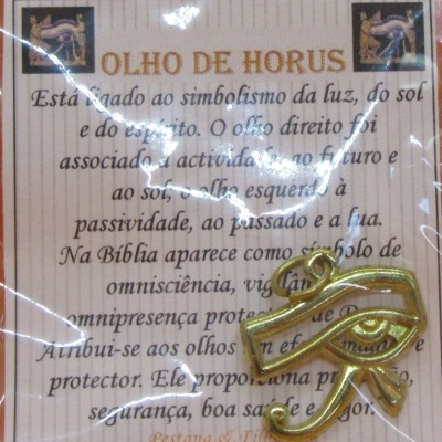 Amuleto dourado Olho de Hórus sobre embalagem com texto explicativo em português europeu