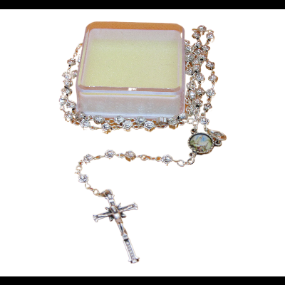 Terço de contas transparentes com crucifixo em cima de caixa pequena branca com líquido amarelado