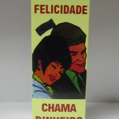 Embalagem amarela com texto 'FLUIDO DA FELICIDADE CHAMA DINHEIRO CONTEÚDO 80ml' e ilustração de casal