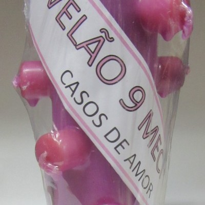 Vela roxa decorativa com nove pontas rosadas embalada em plástico transparente.