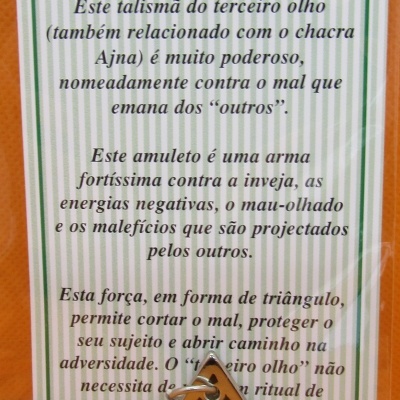Amuleto triangular dourado com símbolos pretos e cartão informativo sobre O TERCEIRO OLHO em português