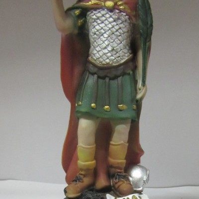 Estátua colorida de S. Expedito com cruz e folha, base marrom com placa e texto