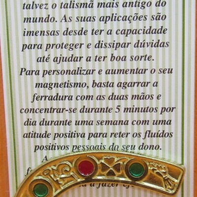 Ferradura da sorte dourada com pedras coloridas e texto explicativo em fundo riscado verde e branco.