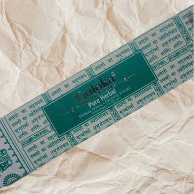 Embalagem de incenso Goloka Pure Herbal azul e branca sobre papel amassado bege
