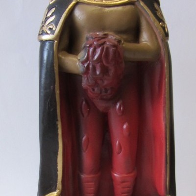 Estátua masculina com capa preta e vermelha segurando coração e caveira ao lado.