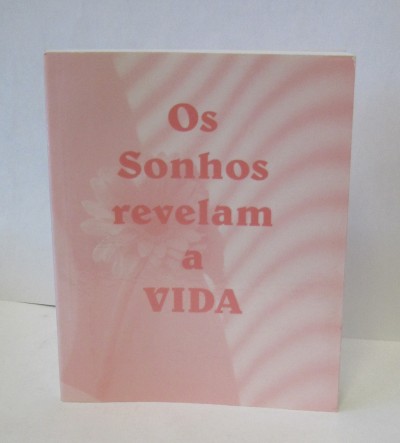 Capa de livro rosa com texto vermelho 'Os Sonhos revelam a VIDA' e sombras de folhas ao fundo.