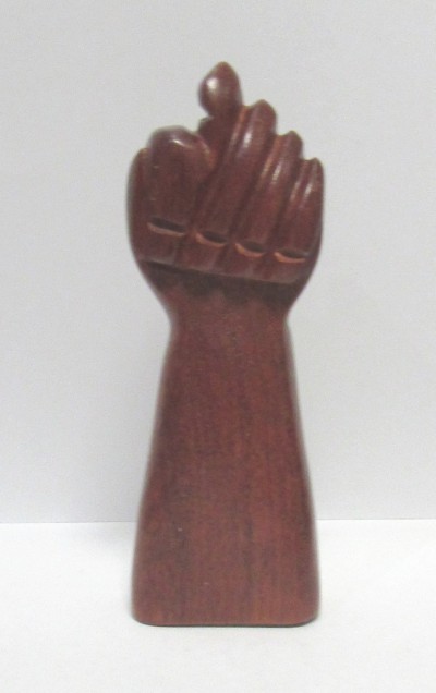Escultura de madeira em forma de punho fechado com polegar sobre os dedos