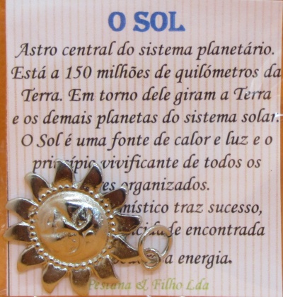 Cartão com texto sobre o Sol e pendente metálico dourado em forma de sol com olho no centro sobre fundo de madeira clara
