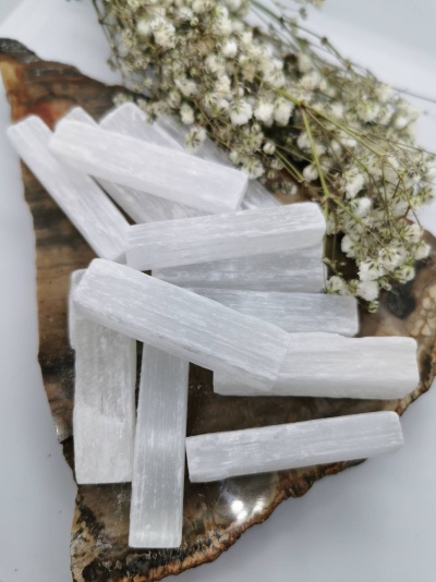 Bastões de selenite branca sobre placa de pedra polida com flores brancas