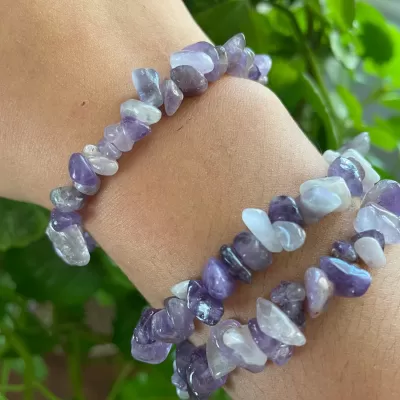 Braceletes de pedrinhas roxas em pulso com fundo de plantas verdes