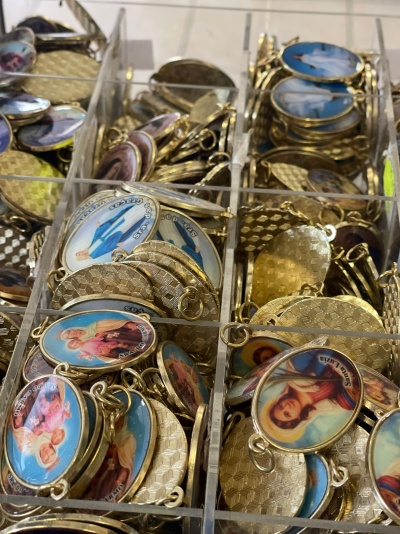 Medalhas religiosas douradas com imagens coloridas organizadas em caixas transparentes