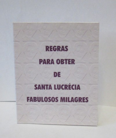 Livro branco com texto 'REGRAS PARA OBTER DE SANTA LUCRÉCIA FABULOSOS MILAGRES'