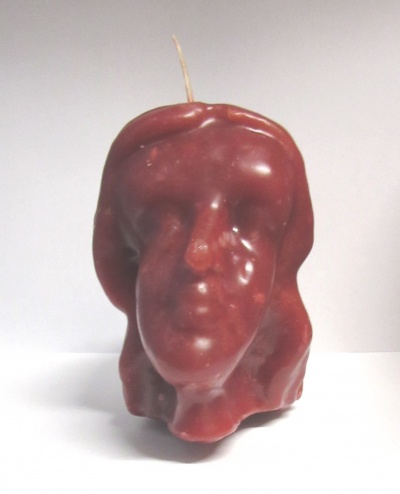 Vela castanho-avermelhada em forma de cabeça humana com pavio no topo