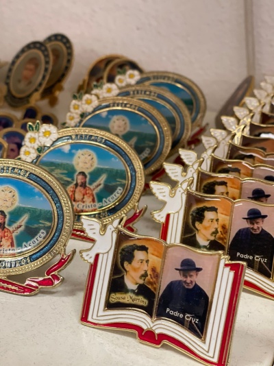 Ímanes religiosos em metal esmaltado com imagens e textos numa prateleira branca