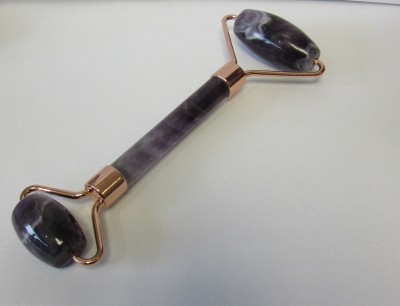 Rolo de massagem facial em pedra roxa com detalhes metálicos dourados