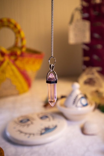 Colar com pendente de cristal cor de rosa e fundo desfocado com cestos e cerâmica