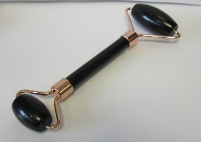 Rolo de massagem facial preto com armação dourada sobre fundo branco