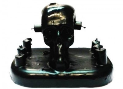 Objeto decorativo preto com crânio e parafusos em base oval