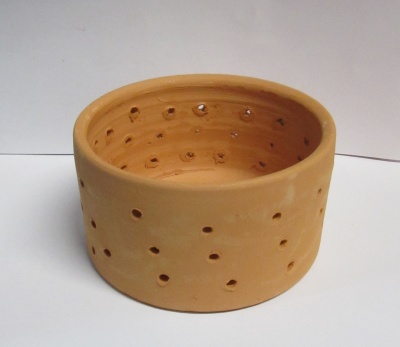 Recipiente de cerâmica castanha com buracos, sobre superfície e fundo brancos