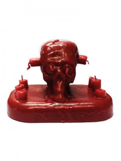 Vela vermelha em formato de caveira com base retangular e vários pavios.