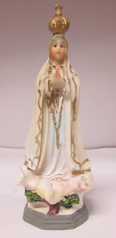 Estátua da Virgem Maria com vestido branco e dourado, coroa dourada e rosário, base cinzenta e vegetação verde