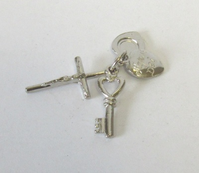 Pendente de cruz, chave antiga e coração em metal prateado sobre fundo branco