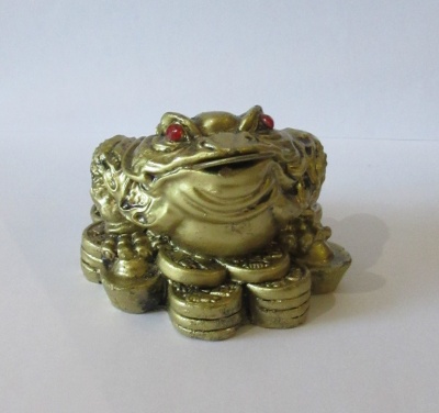 Figura de sapo dourado com olhos vermelhos e moedas, sobre fundo branco