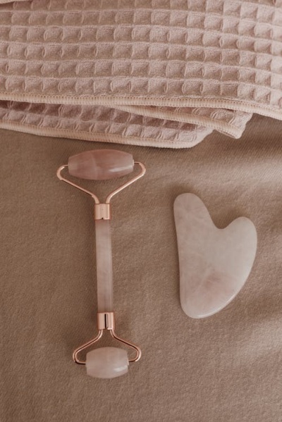 Rolo facial e pedra Gua Sha rosa claro em tecido bege com toalha rosa ao fundo