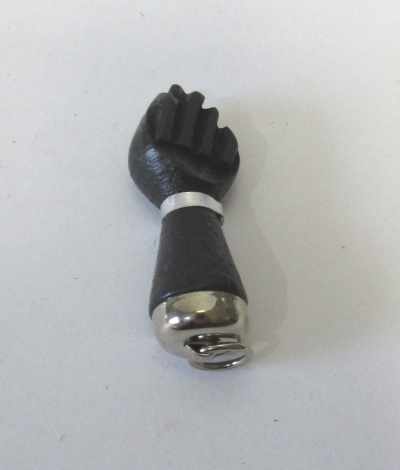 Peça em forma de punho fechado preta com base prateada sobre fundo branco.